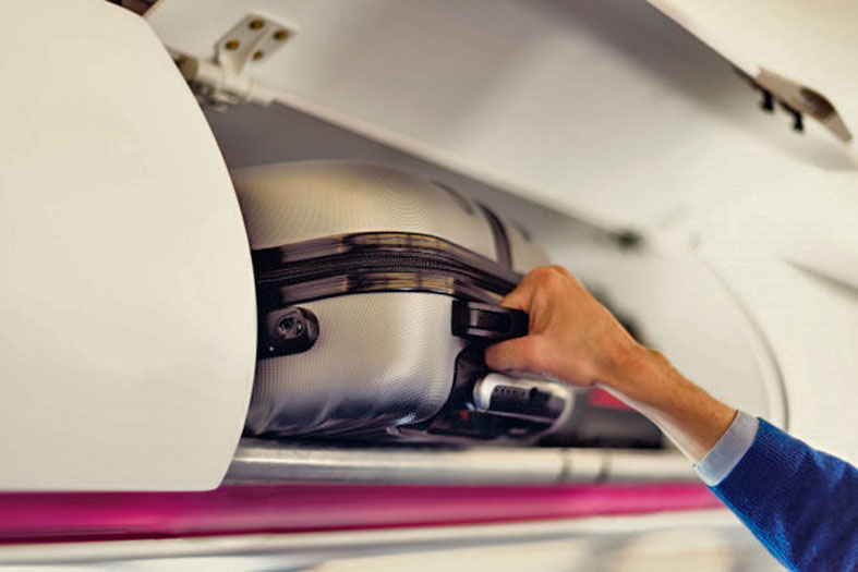 uma mão colocando uma mala no bagageiro de uma aeronave