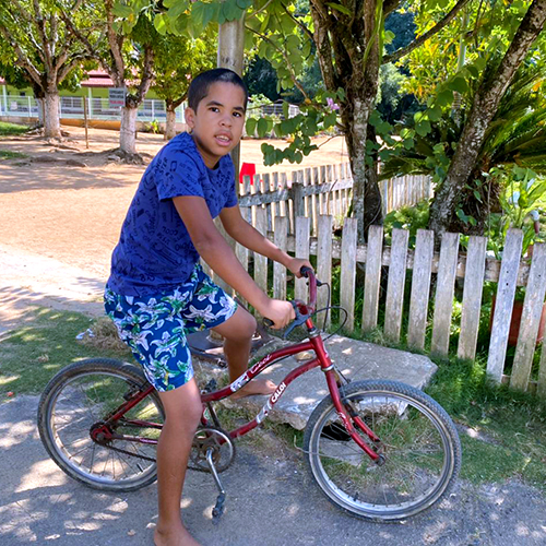 menino de pele parda, estatura mediana, cabelos pretos e camisa azul escura com bermuda estampada.