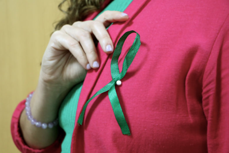 Mulher apontando para fitinha verde em sua blusa, simbolizando a conscientização dos cuidados com a saúde mental.