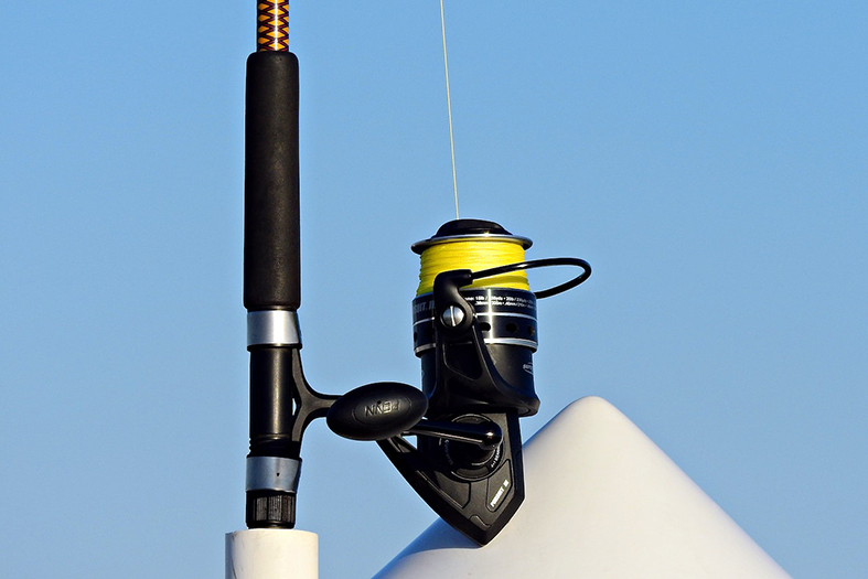 Molinete e parte de uma vara de pesca sob fundo azul do céu.