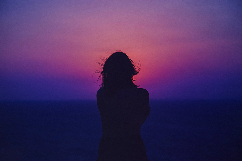 silhueta de uma mulher contrastando com um pôr do sol púrpura.