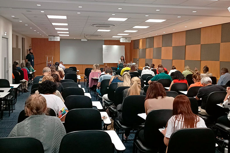 Auditório cheio de pessoas fazendo prova escrita.