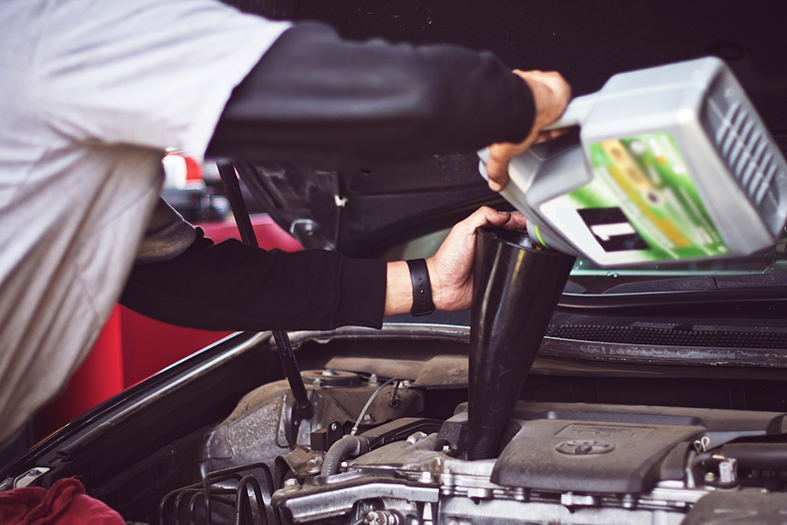 Funcionário troca óleo do motor de um carro.