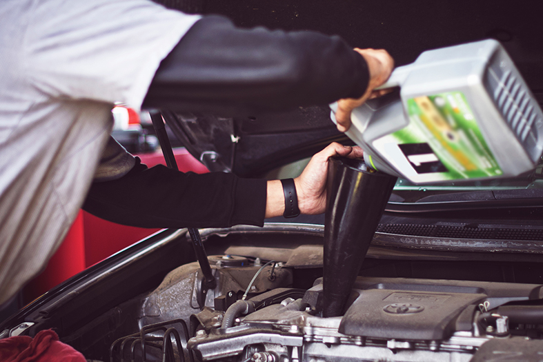 Funcionário troca óleo do motor de um carro.