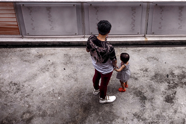 Pai e filho pequeno parados em um pátio cujo piso de cimento está manchado de preto.