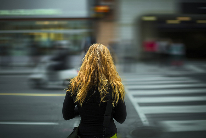 mulher de cabelos ruivos de costas espera para atravessar uma movimentada avenida.