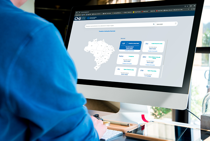 Vista de costas, uma pessoas de camisa azul usa um computador.