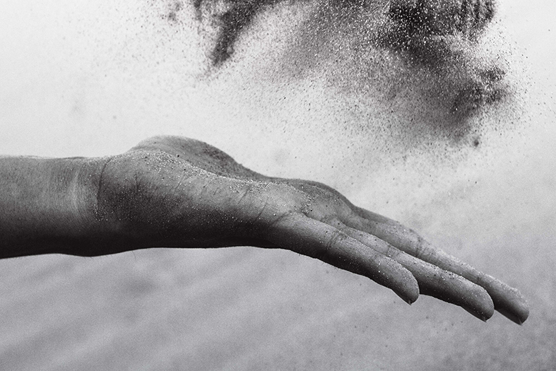 Foto preto e branco de uma mão jogando poeira ao ar.