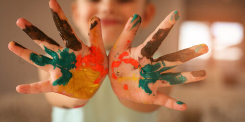 Menina mostrando as mãos sujas de tinta.