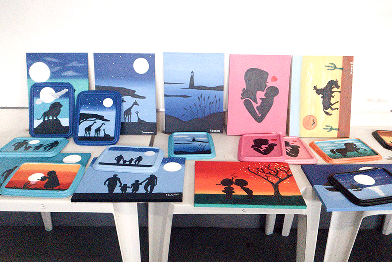 Trabalhos artísticos dispostos em exposição sobre uma mesa.