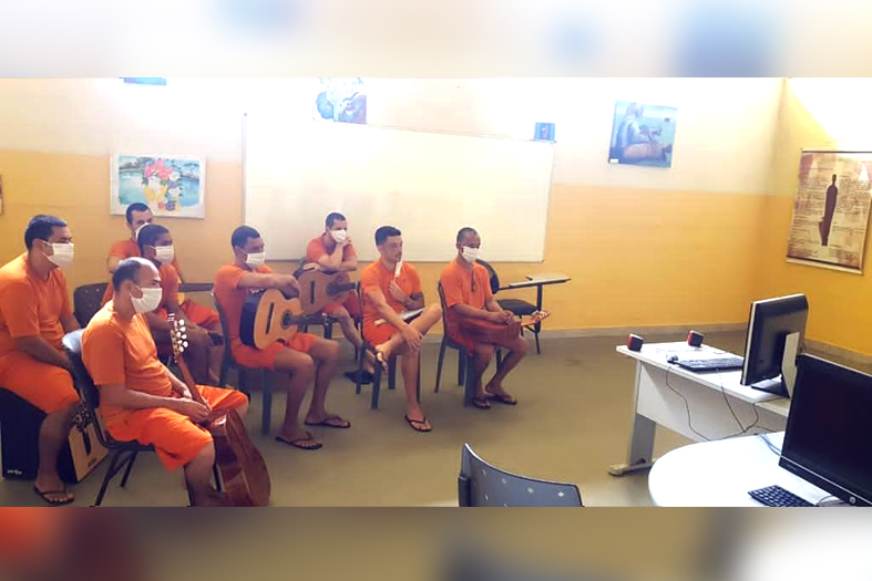 12 internos da penitenciária semiaberta de vila velha usando máscaras e reunidos em uma sala. um deles está tocando um violão. todos eles fazem parte do projeto tocando em frente.