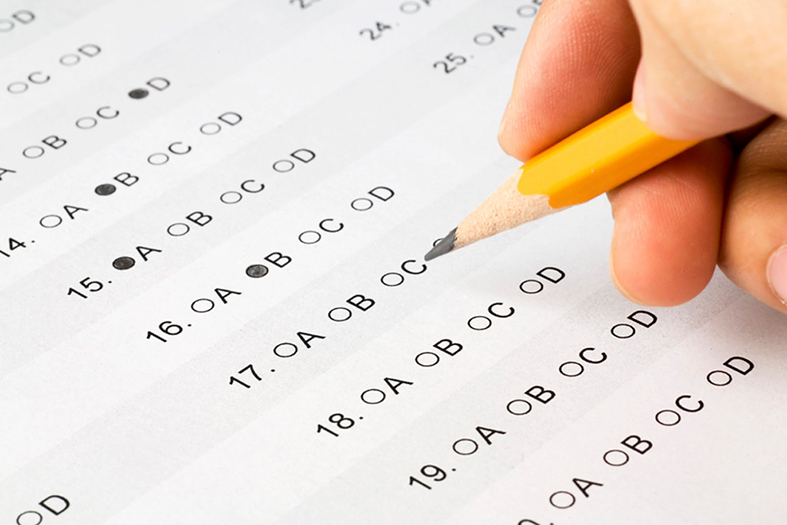 Detalhe de uma m"ao segurando um lápis e marcando questões em uma prova de múltiplas escolhas.