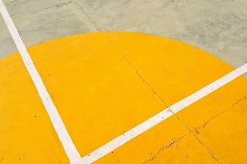 Detalhe de quadra de esportes com piso pintado de amarelo e branco.