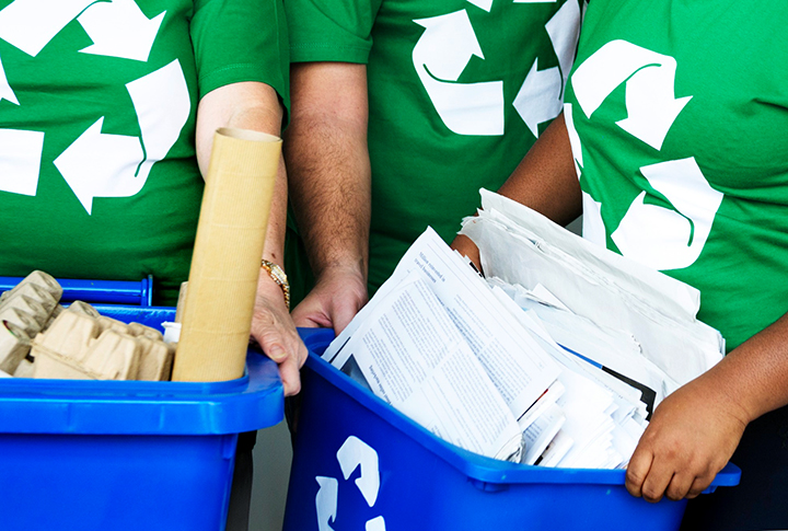 Três pessoas segurando recipientes com papéis para a reciclagem.