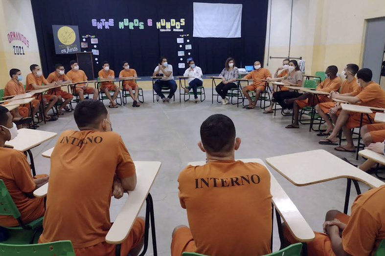 grupo de reeducandos do sistema prisional sentados em cadeiras formando um círculo assiste a uma