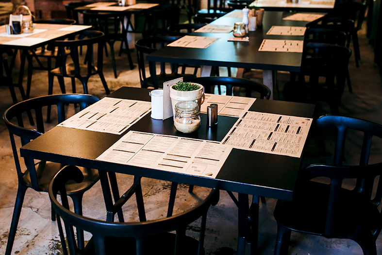 Mesa de restaurante na cor preta com toalhas de papel e copos com mohos e canudos.