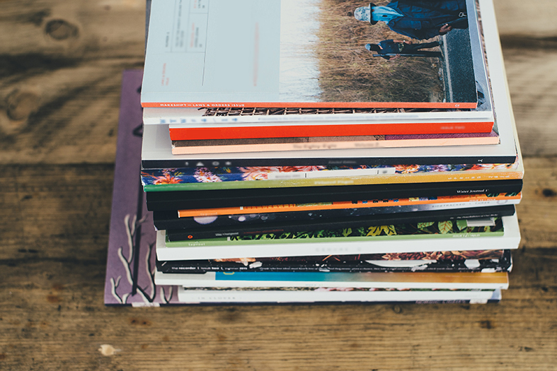 Uma pilha de revistas variadas sobre uma mesa de madeira.