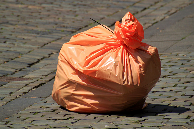 Saco de lixo na cor laranja deixado sozinho em calçada.