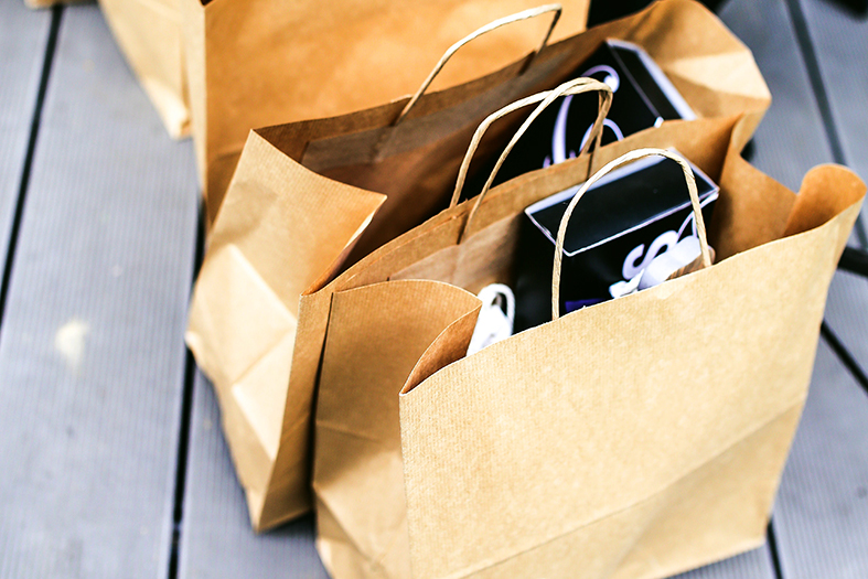 Sacolas de papel pardo com caixas de presentes dentro repousam sobre chão de cor cinza.