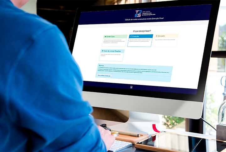 Homem usando um computador desktop. Na tela vê-se a página inicial do Sistema de Custas do TJES.
