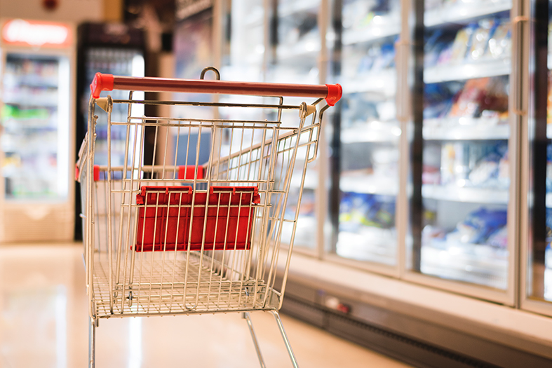 Seção de frios/congelados de um supermercado onde vemos um carrinho vazio.