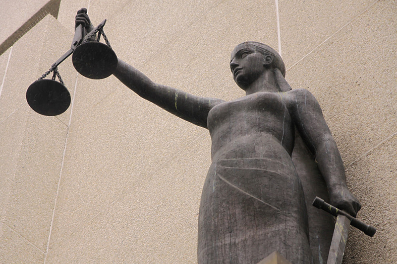 deusa Themis que representa a justiça. Ao fundo da estátua uma parede externa de um prédio