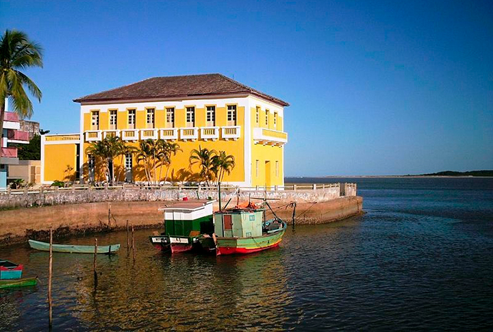 Imagem do ponto turístico conhecido como Trapiche, um prédio antigo na cor amarela, em Conceição da Barra/ES.