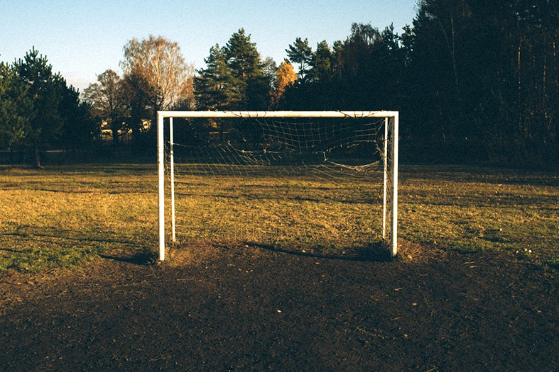Trave de futebol na cor branca em um campo de gramado falhado.