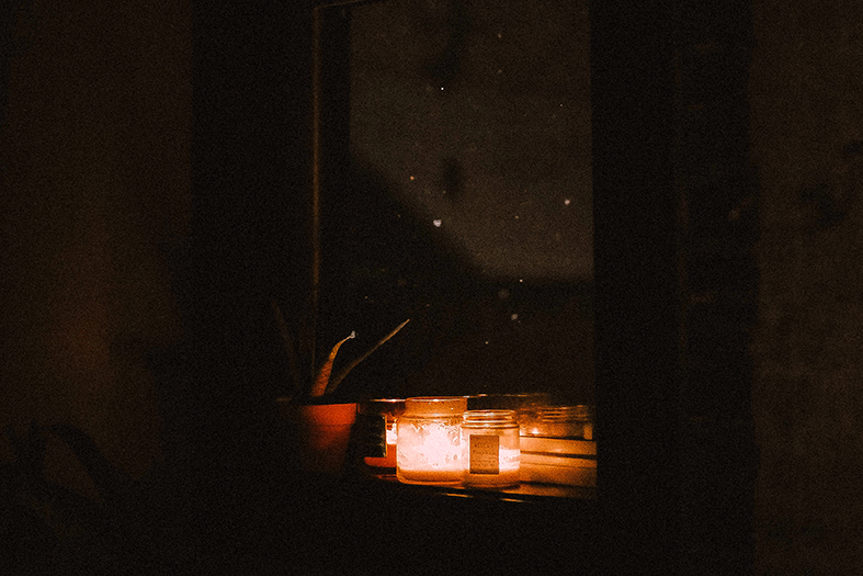 velas em potes de vidro em uma janela de um cômodo escuro.