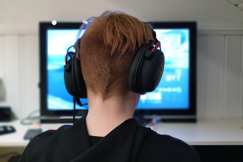 adolescente de costas, usando um fone de ouvido, olha para um monitor